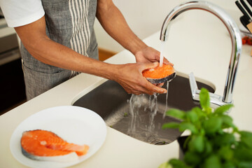 African man rinsing ingredients for nutritious salmon dish at kitchen