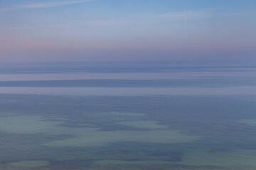 Blue sky with haze and blurry glowing pink clouds above the sea. Shallow coastal sea water with azure patterns. Ripples in the water