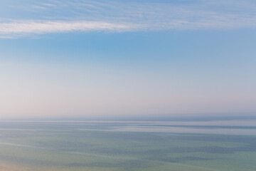 Blue sky with haze and blurry glowing pink clouds above the sea. Shallow coastal sea water with azure patterns. Ripples in the water