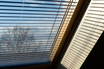 Half lowered window blinds in front of the blue sky