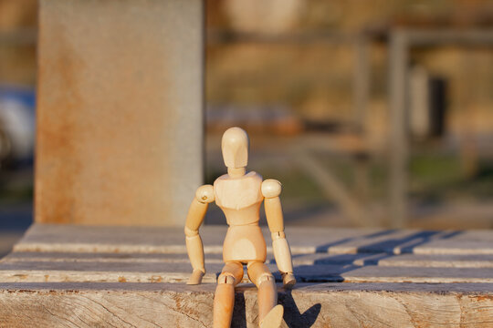 A wooden mannequin sits alone on a bench in the rays of the sunset.