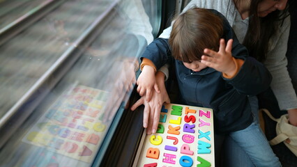 Child and mother doing homeschool activity while traveling by train. Mom teaching son colorful...