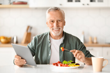 Happy Older Man Having Breakfast And Using Digital Tablet In Kitchen