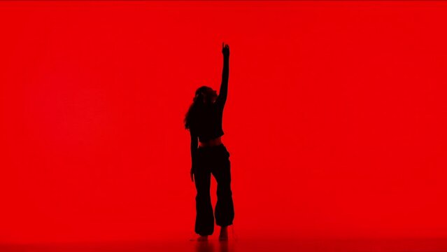 Attractive girl silhouette in black outfit dancing elements of contemporary modern dance on red background in studio.