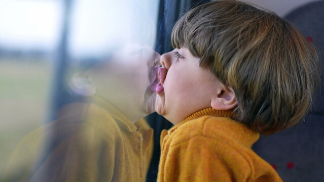 Bored funny small boy with face glued on trian window. Mouth and lips pressed on glass and staring at landscape scenery pass by in transportation