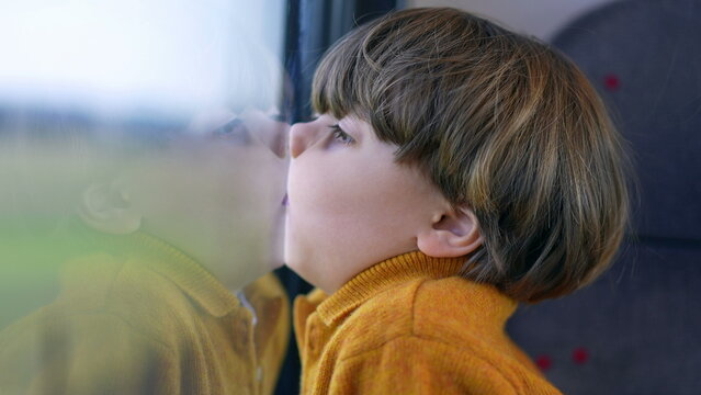 Bored funny small boy with face glued on trian window. Mouth and lips pressed on glass and staring at landscape scenery pass by in transportation
