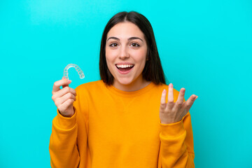 Young caucasian woman holding invisible braces isolated on blue background with shocked facial...