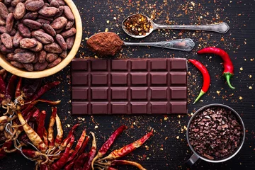 Fotobehang Dark chocolate bar, red hot chilli pepper cayenne,  dry hot chili spices, cocoa beans nibs powder, food tasty design on black wooden background © ValentinValkov