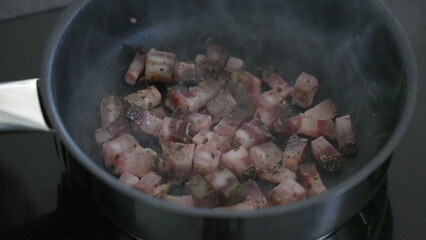 Cooking pieces of bacon inside pan, close-up greasy food preparation for morning breakfast routine