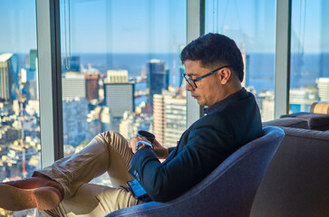 Young businessman sitting in a luxurious office looking at his watch with a beautiful view of the...