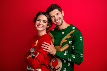 Portrait of two peaceful lovely partners cuddle toothy smile wear festive ugly sweater isolated on red color background