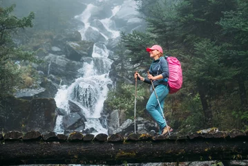 Foto auf Acrylglas Makalu Young woman with backpack and trekking poles crossing wooden bridge near power mountain river waterfall during Makalu Barun National Park trek in Nepal. Mountain hiking and active people concept image