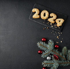 Cookies with peanuts in the form of numbers 2024 on the dark background decorated with pine twig and christmas toys.