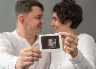 A pregnant woman and her husband are holding in their hands a photo of their future newborn baby. Pregnancy, motherhood