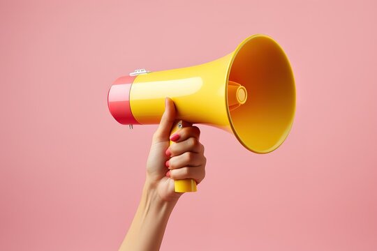 female hand holding a hot yellow megaphone over pink background