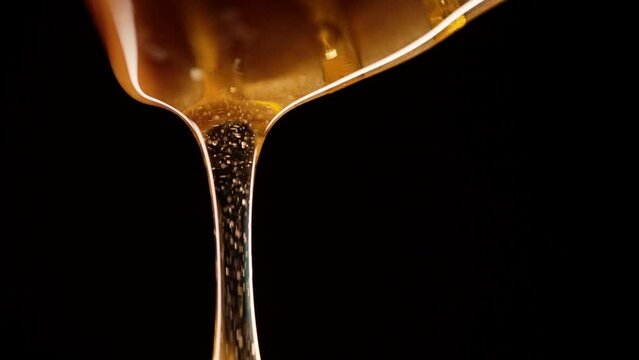 Organic honey flows, wooden dipper stick on black background. Fluid nectar, slow