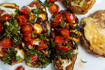 Grilled eggplants stuffed with cherry tomatoes, herbs and cheese are laid out on white platter.