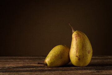 two ripe pears lie on a wooden table against a soft background of a dark beige wall. side view. selective focus. artistic rustic photo with copy space