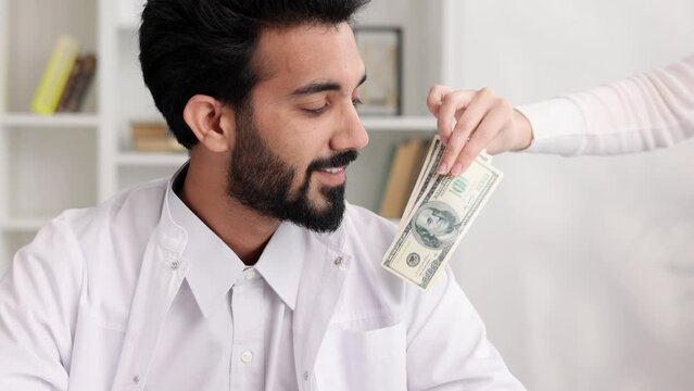 Corruption in medicine, an Indian doctor is happy to take a bribe. The patient's hand puts money in the doctor's pocket.