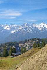 Eine Hütte in den bayerischen Voralpen mit schneebedeckten Bergen im Hintergrund.