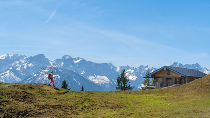 Auf dem Staffel Berg in den Bayerischen Voralpen läuft eine Wanderin zu einer Hütte mit...