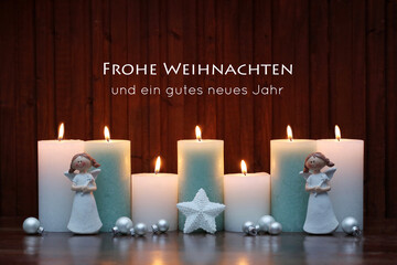 Brennende Kerzen mit Engelsfiguren und dem Text Frohe Weihnachten und ein gutes neues Jahr.