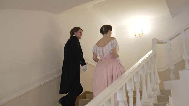 A couple in 19th century costumes. A man and a woman in 19th century costumes walk around the palace. The guy and the girl in the images of the 19th century climb the stairs.