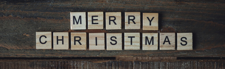 Minimalistic holidays card on wooden background, rustic zero waste decorations. Sustainable lifestyle. Merry Christmas greeting written with wooden blocks. Banner