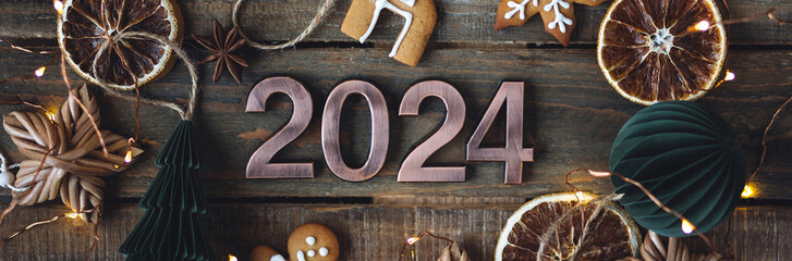 Banner. 2024 Christmas or New Year composition. Holidays card on wooden background with gingerbread cookies, handmade craft toys, rustic zero waste decorations. Sustainable lifestyle, natural elements