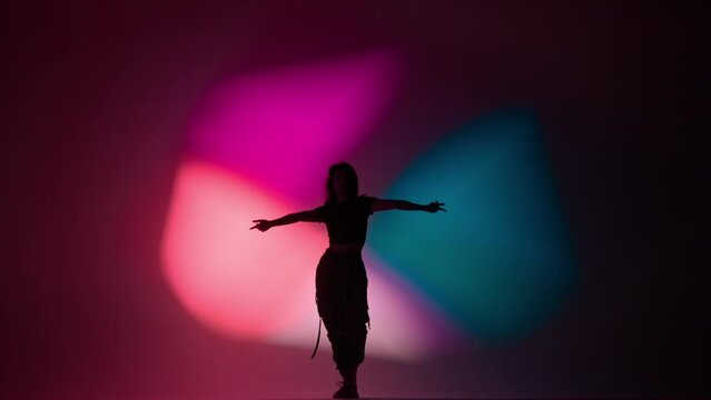 Attractive woman in pants and top dancing dynamic jazz funk dance, isolated on purple pink blue background neon light.