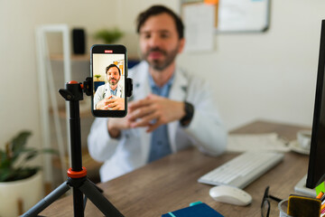 Hispanic doctor streaming using his smartphone or filming an online video for his patients or...