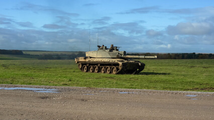 Fototapeta premium close-up of Commander and gunner directing a British army FV4034 Challenger 2 ii main battle tank moving across a grass field at speed, on a military exercise, Wiltshire UK
