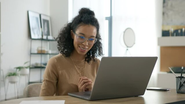 Portrait of happy multi ethnical woman looking at laptop screen indoors. Elegant businesswoman in glasses chatting online. Positive young business woman using computer for online interview or training