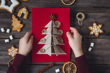 Concept of christmas leisure, family time, do it yourself present. Little boy holding handmade card made with recyclable natural materials, zero waste, sustainable lifestyle, hobby