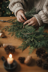 Making Christmas rustic wreath. Hands holding cedar branches, making wreath on wooden table with...