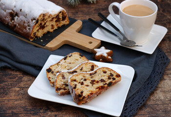 Christmas stollen cut into pieces on a plate with a cup of coffee: traditional cake for Christmas with raisins and powdered sugar