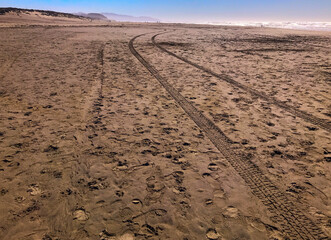 View of tire tracks in the sand of Ocean Beach in San Francisco, California on a sunny day in late fall. The Pacific Ocean is visible on the right.