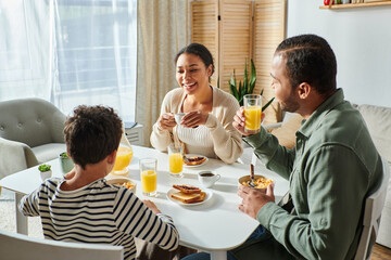 cheerful modern african american family having breakfast together and smiling at each other