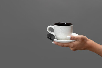 Close up on female hand, holding cup of coffee or espresso against grey background