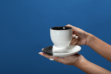 Close up on female hand, holding cup of coffee or espresso against blue background