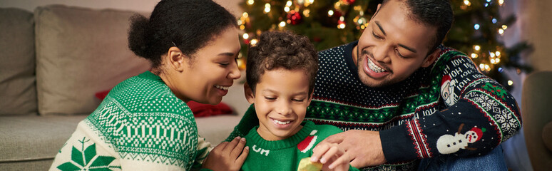 cheerful african american family in cozy sweaters smiling and hugging lovingly, Christmas, banner