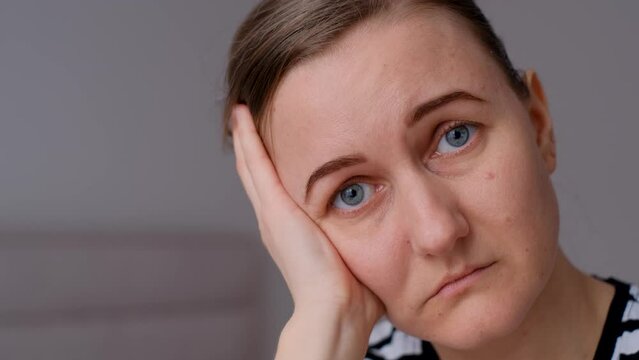 Lonely young woman sitting on bed. Depressed woman at home looking sadly at camera. Close up.