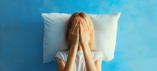 Upset sad crying woman covering her eyes with her hands lying on the pillow while experiencing...