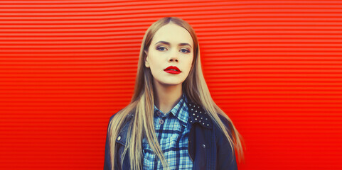 Fashionable portrait of beautiful blonde young woman posing in black rock leather jacket on red background