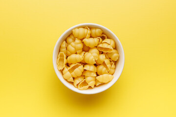 Uncooked gnocchi pasta. Raw italian pasta in bowl on yellow background.