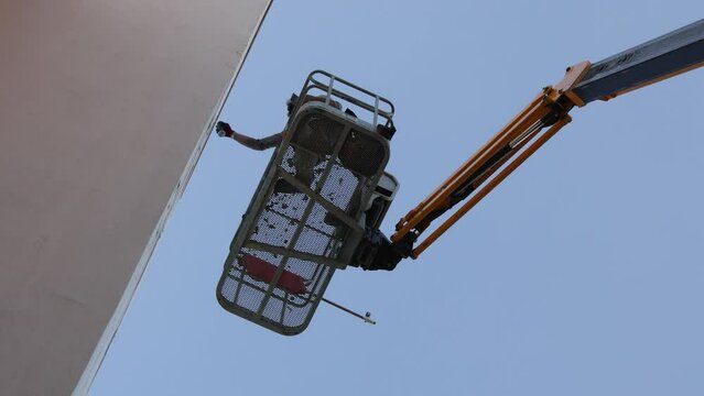 Graffeur peignant un mur &agrave; la bombe sur une nacelle, en contre plong&eacute;e