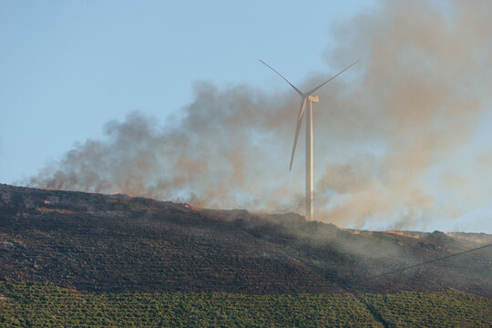 Bush fire on top of a hill with smoke in the air besides wind turbines, Arouca, Portugal