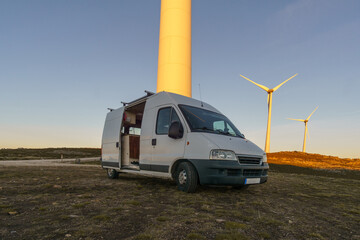 Wind turbines at Serra da Arada over mountain landscape at evening sunset with camper van in...