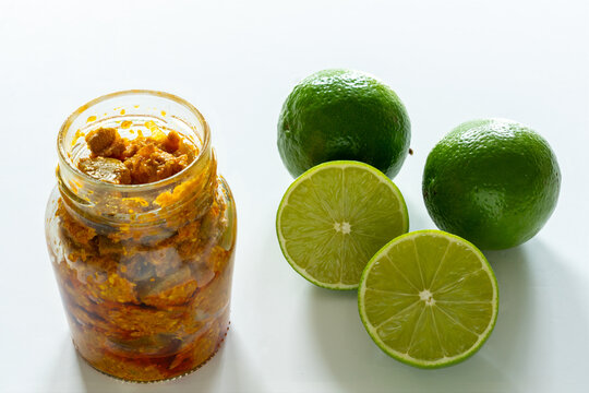 Homemade Indian spicy lime pickle with salt, chilli, pepper in a glass jar againt a white background.