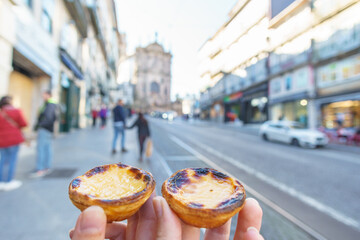 Tow Hand with Portugal's traditional sweet dessert Pastel de nata egg custard tart pastry with street in Porto, Portugal - obrazy, fototapety, plakaty
